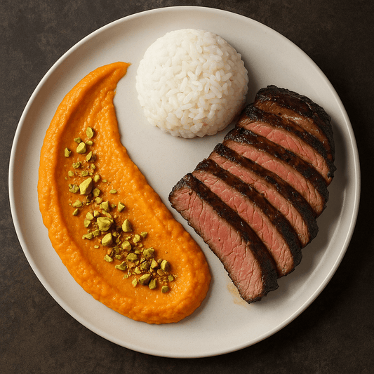 Sliced grass-fed ribeye served with carrot-pistachio purée and buttered rice on a plate.