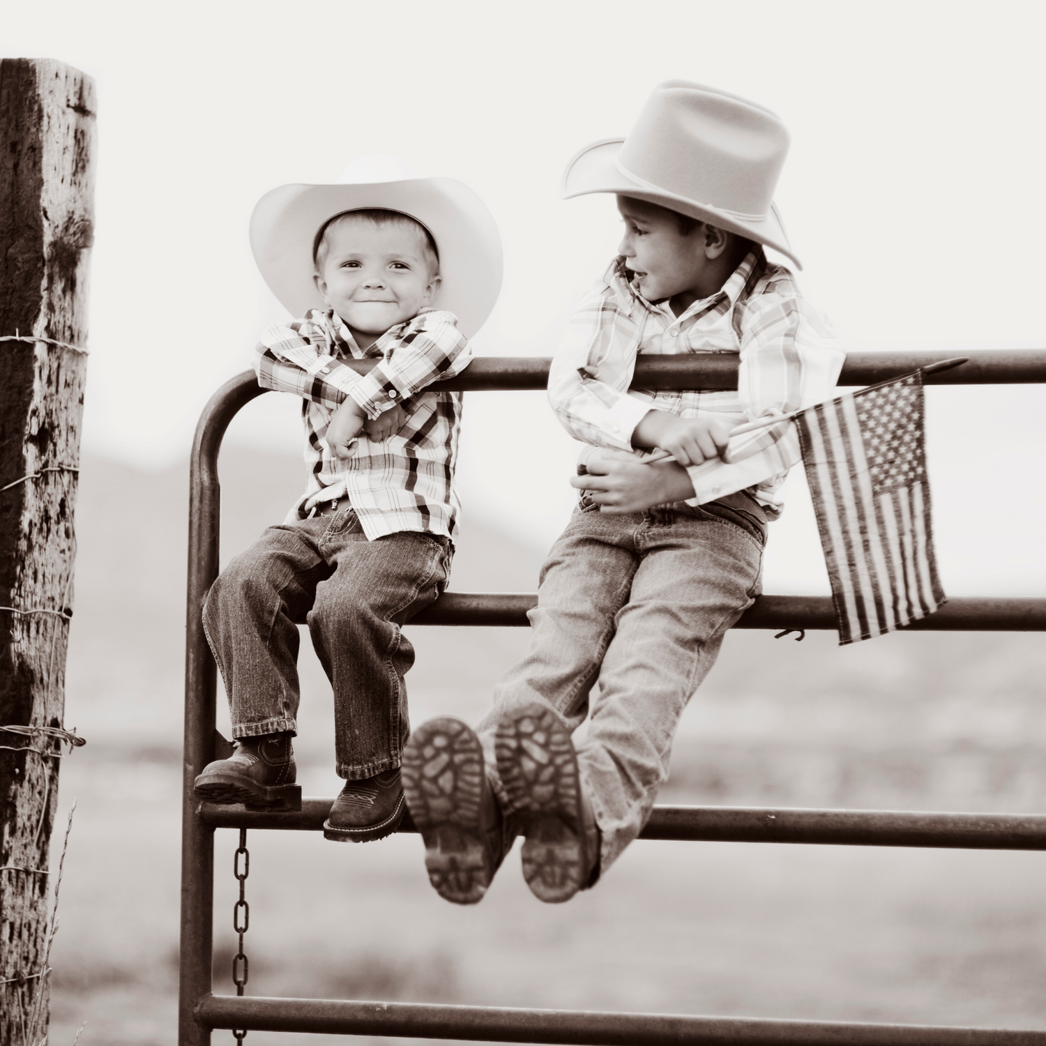 Two young boys in cowboy hats sitting on a fence, showcasing a rustic ranch lifestyle.
