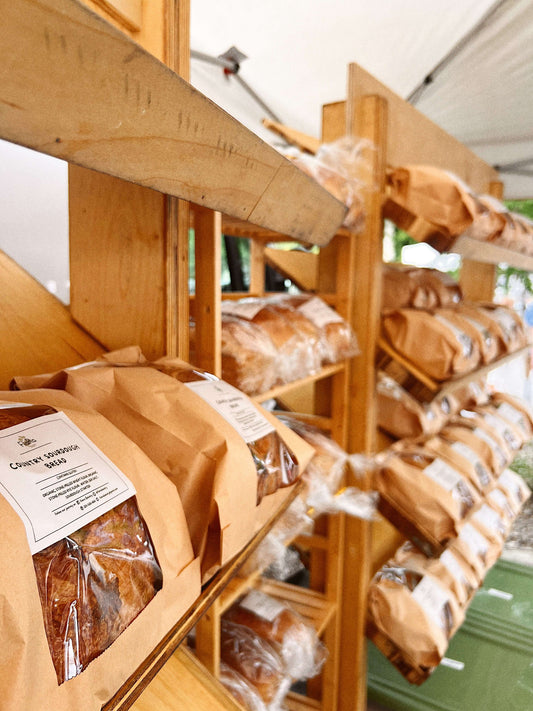 🍞 FlaRa Sourdough (1 loaf) displayed on wooden shelves at a market.