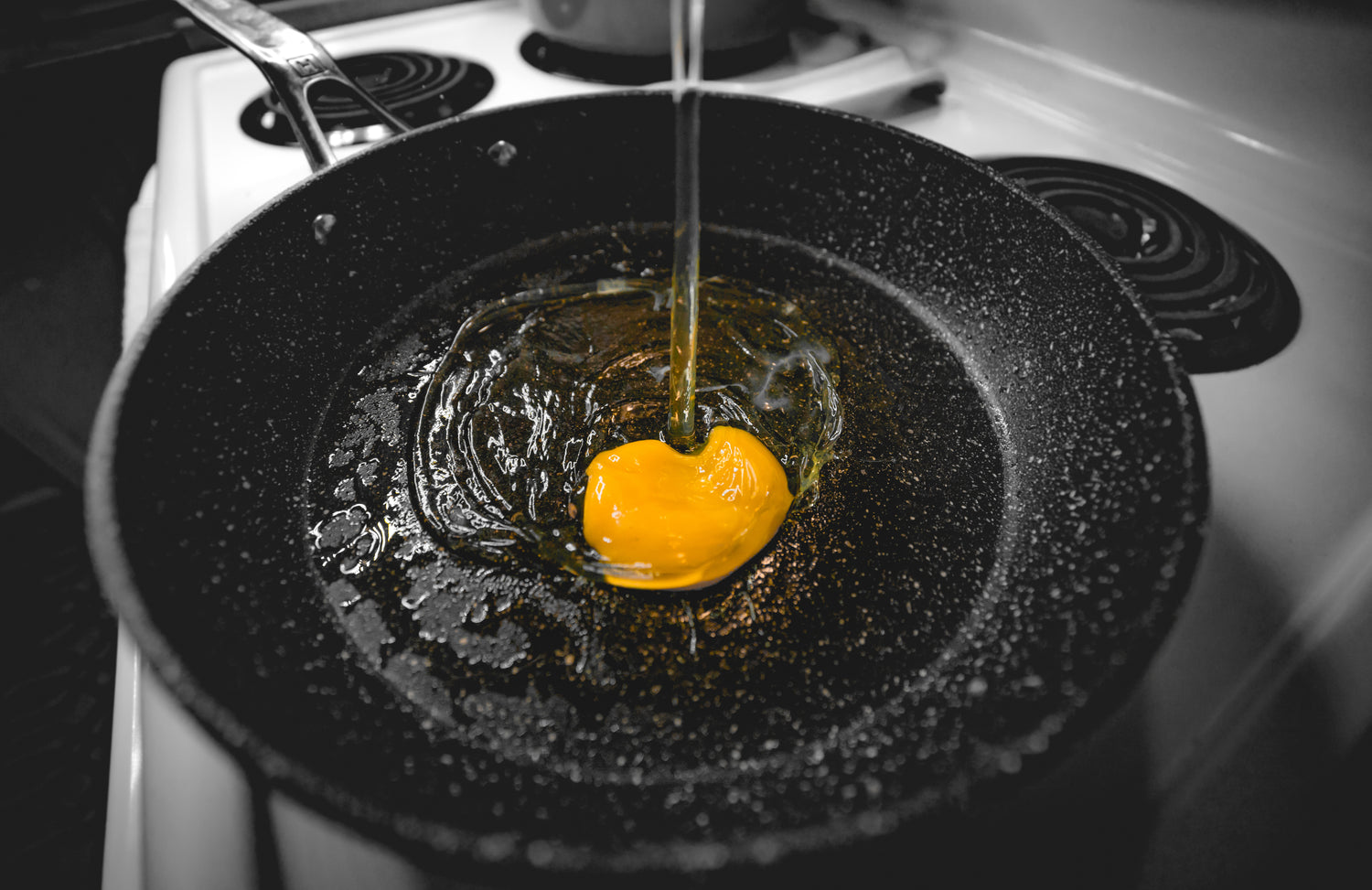 Egg yolk breaking into a hot pan, preparing for a delicious meal with farm-fresh ingredients.