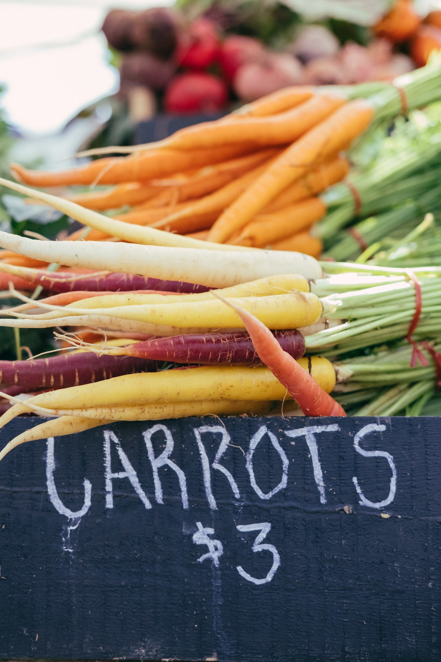 Fresh carrots in various colors, priced at $3, displayed at a local farm market.