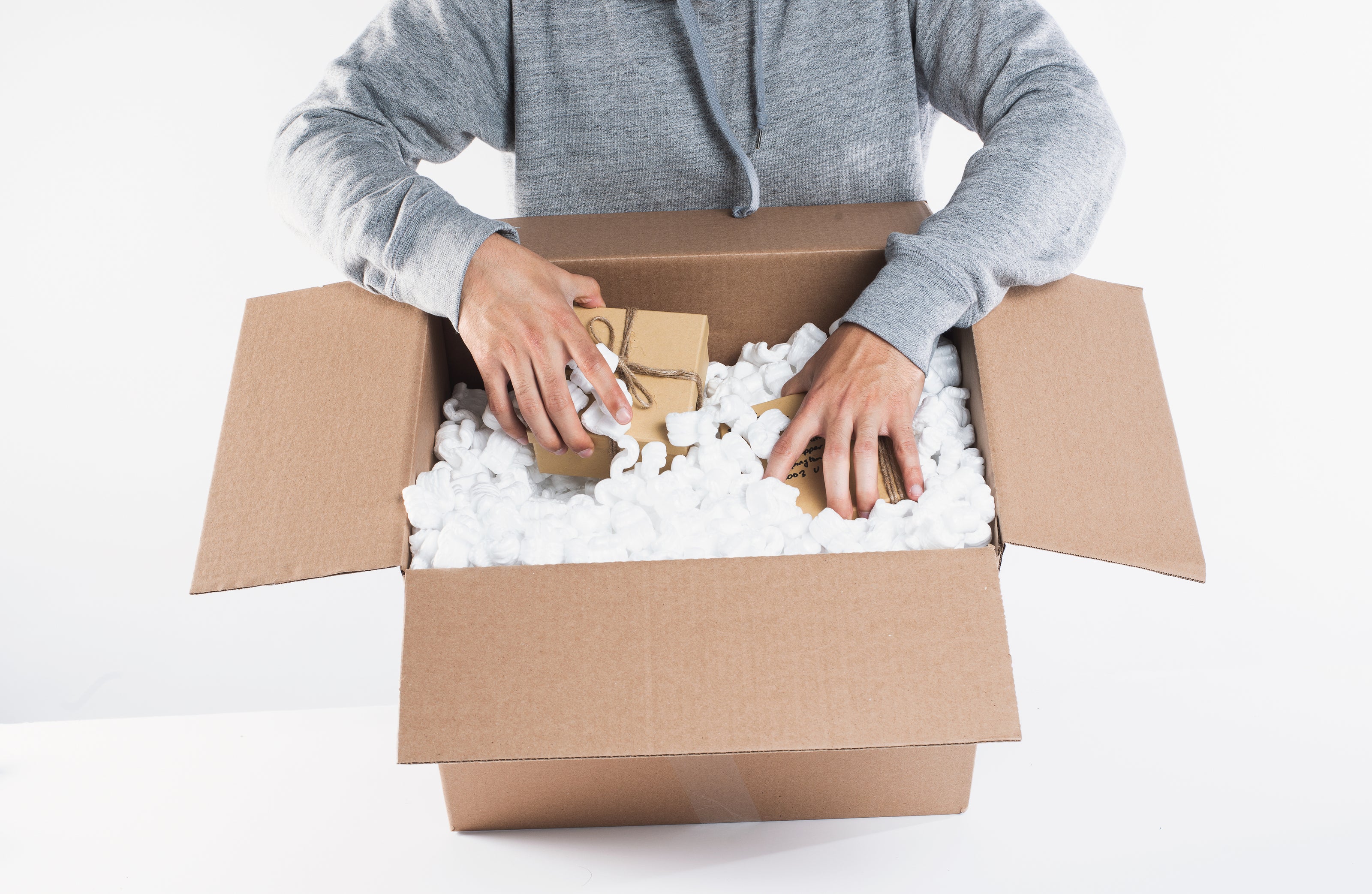 Person unpacking a cardboard box filled with packing peanuts and small packages for delivery.