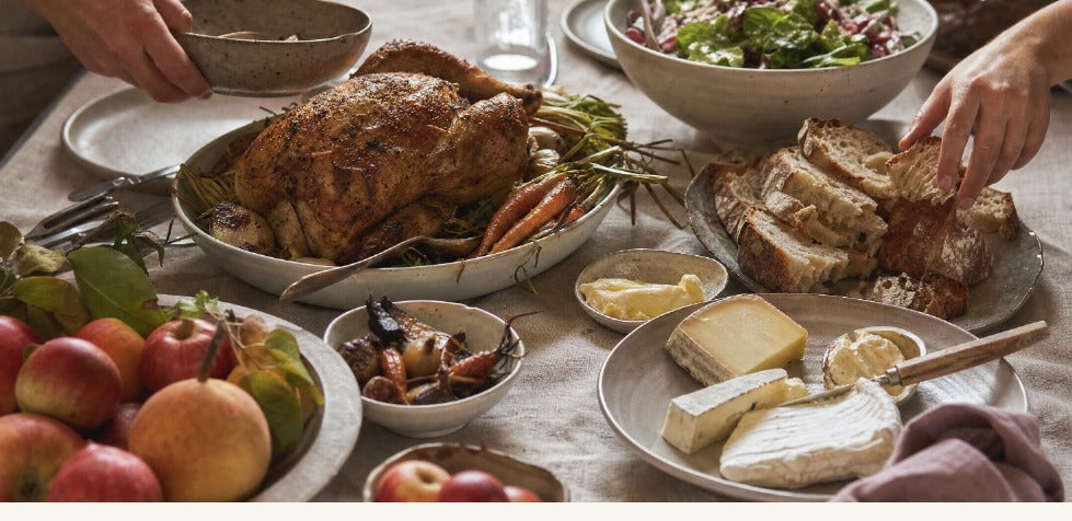 A seasonal table set with roast chicken, sourdough, cheeses, fruit, and greens